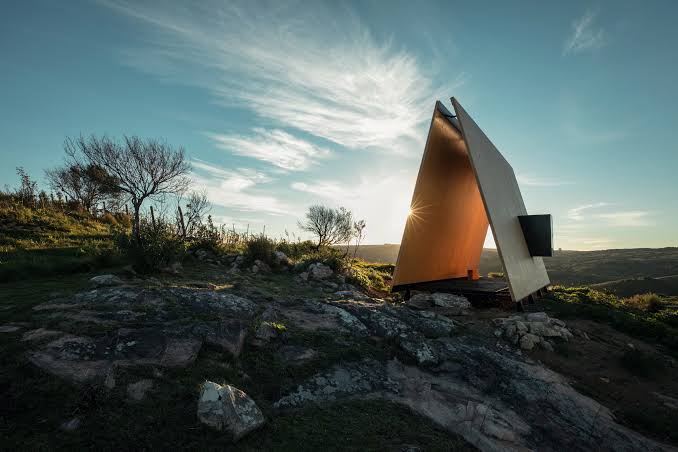 Dark clad shelter with a curved glass wall on a hillside among Uruguayan vineyards